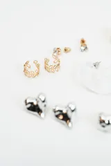 Set de aros variados que incluye aros tipo argolla dorados, aros con piedra brillante, aros tipo argolla de acrílico transparente, aros con diseño de hojas y aros con forma de corazón plateado.