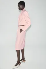 Blazer corto rosado con cuello solapa, hombreras y mangas largas. Cuenta con cierre cruzado delantero con dos botones oscuros y un bolsillo de ojal en el pecho.