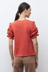 Remera de algodón color terracota con cuello redondo y mangas cortas con detalle de volados escalonados y costuras decorativas.