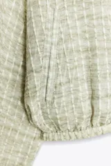 Cazadora de cuello redondo y manga larga, color verde claro con patrón a cuadros. Confeccionada en tejido de organza con estructura y acabados elásticos. Cierre frontal con cremallera y bolsillos delanteros.