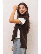 Chaleco tejido de punto color marrón, con cuello levemente alto, silueta amplia y aberturas laterales. Presenta un diseño de largo asimétrico, siendo más corto en el frente y más largo en la espalda.