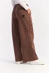 Pantalón de corte ancho y relajado en color marrón, con cintura elástica, bolsillos laterales y costuras verticales decorativas en contraste a lo largo de las piernas.