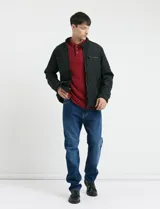 Remera de manga larga con cuello polo, confeccionada en tejido de punto canalé francés. Presenta abotonadura frontal con botones de madera y detalles a contratono en la cartera y el interior del cuello.