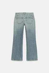 Jeans de tiro bajo con corte flare, confeccionados en denim azul con lavado localizado. Presentan bolsillos de plastrón en el frente, trabillas para cinturón y cierre frontal con cremallera y botones metálicos.