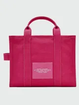 Cartera tipo tote bag de Marc Jacobs, confeccionada en lona color beige con el logo estampado en blanco al frente. Cuenta con doble asa superior, correa de hombro ajustable y extraíble, y cierre superior con cremallera.