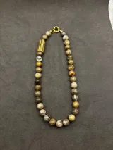 Collar de cuentas de piedras naturales en tonos tierra, con detalles de tubos dorados en los laterales.