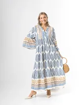 Maxi vestido largo de fibrana en color blanco con estampado paisley y geométrico en tonos azules y tostados, con escote en V, mangas largas amplias y diseño holgado con volados en la falda.