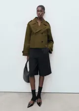 Chaqueta corta de doble botonadura en color verde militar, con cuello de solapa, bolsillos laterales, trabillas en los hombros y mangas largas con puños abotonados.