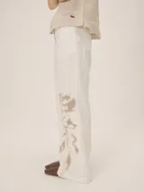 Pantalón de lino rojo de corte ancho, tiro medio con cintura estructurada y cierre frontal con botón, con un sutil estampado floral tono sobre tono en la parte inferior de la pierna izquierda.