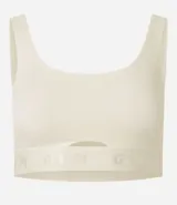 Top deportivo color blanco hueso, de corte ajustado, con breteles anchos y banda elástica inferior con inscripción. Presenta un pequeño recorte circular en el centro del busto.