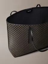 Cartera tote Calvin Klein de diseño estructurado, color negro y marrón con estampado de monograma CK en toda la superficie. Cuenta con asas de mano dobles y finas, y viene acompañada de una mini cartera lisa con cierre y detalle del logo de la marca en dorado.