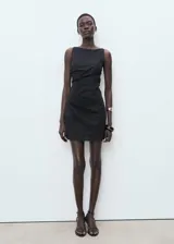 Vestido corto sin mangas de color negro, con cuello barco y diseño drapeado en la cintura. Confeccionado en una mezcla de lino y algodón con forro interior.