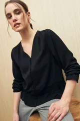 Camisa negra de manga larga con escote en V y botones forrados al tono en el frente. Destaca por su textura sutil y por el detalle de frunces con volados en la parte inferior.