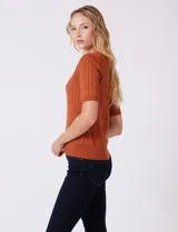 Buzo tejido marca Tahari, color verde, con cuello a la base, manga corta y diseño de ochos en el frente.