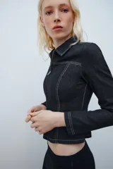 Camisa de denim negra con cuello solapa, manga larga, pespuntes a contraste y cierre frontal con cremallera metálica.