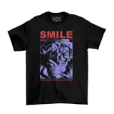 Remera negra de algodón con estampa frontal gráfica que muestra al personaje Joker sosteniendo una cámara fotográfica, acompañada por el texto 'SMILE' y 'THIS COULD BE YOUR LAST TIME'.