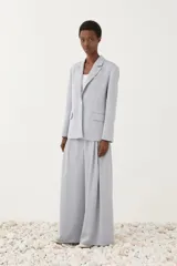 Blazer de corte recto con solapas, cierre de botón frontal y bolsillos con solapa. Cuenta con mangas largas y un gran moño en la espalda como detalle principal.
