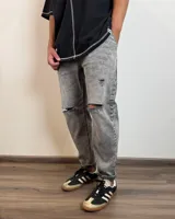 Jean de corte slouchy en color gris con efecto lavado, presenta roturas en las rodillas y dobladillo en los tobillos.