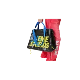 Bolso tipo shopping bag color negro de Eme Studios, con estampado frontal grande en amarillo y azul que incluye las palabras "EME STUDIOS" y detalles de estrellas. Cuenta con asas de mano azules con inscripciones de la marca y cordones ajustables en los laterales.