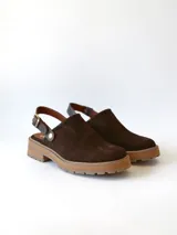 Zueco de cuero gamuzado color chocolate, con diseño de punta cerrada y tira ajustable con hebilla metálica en el talón. Presenta una suela de plataforma dentada en tono marrón claro.