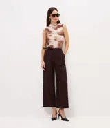 Pantalón de sastrería color marrón oscuro, de corte recto y tiro alto, confeccionado en crepé. Incluye trabillas en la cintura y un cinturón fino de poliuretano con hebilla metálica.