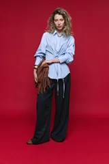 Camisa blanca de manga larga con volumen y estructura, cierre frontal con botones y lazo ajustable en la cintura que realza la silueta.