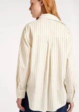 Camisa de manga larga con cuello clásico y cierre frontal con botones. Presenta un diseño a rayas verticales en tonos beige y crema.