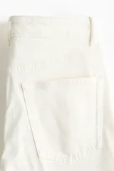 Jean tobillero de corte slim straight y tiro alto, en denim de algodón blanco con ligero stretch, cinco bolsillos, cierre de botón y cremallera, y pliegues marcados al frente y en la espalda.