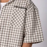 Camisa de manga corta de popelina con patrón a cuadros, calce boxy y largo a la cintura, con bolsillos y canesú cortados en diagonal.