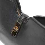 Cartera estructurada mediana de cuero sintético negro, con asa corta fija y correa larga regulable y desmontable. Presenta un broche giratorio metálico en el cierre superior y un detalle de herraje metálico dorado en el frente, con el logo XL aplicado.