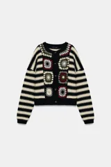 Chaqueta de punto con cuello redondo y manga larga, que combina un diseño de rayas horizontales en blanco y negro con paneles frontales decorados con motivos de crochet en tonos tierra y granate. Presenta cierre frontal con botones.