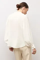 Camisa blanca de corte recto con cuello mao, cierre frontal de botones y mangas largas abullonadas con puños ajustados.