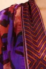 Cover up largo tipo túnica con escote en V, mangas tres cuartos y lazo ajustable en la cintura. Presenta un estampado vibrante de hojas en tonos púrpuras y cobrizos con detalles geométricos en los bordes frontales.