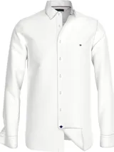 Camisa blanca de corte regular Tommy Hilfiger, confeccionada en algodón dobby Oxford. Tiene cuello con botones, cierre con botones, puños redondeados con dos botones, botón final a contraste y logo de Tommy Hilfiger bordado en el pecho.