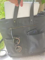 Mochila negra de cuero convertible en bolso de mano o bandolera. Tiene compartimento para laptop, bolsillos exteriores y correas ajustables y extraíbles.