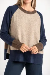Sweater de tejido de punto con diseño color block. Cuerpo principal en beige jaspeado, mangas y puños en azul marino, y detalles en marrón en el cuello y puños.