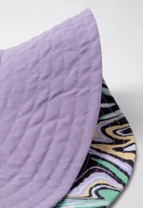 Gorro tipo bucket hat estampado con flores y hojas en tonos verde y celeste sobre fondo blanco. Es reversible.