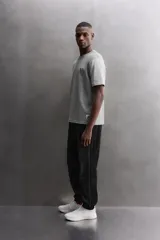 Camiseta relaxed fit de algodón, color gris melange con mangas en un tono de gris más claro. Tiene cuello redondo, manga corta, bordado frontal y texto estampado en la espalda a contraste. Incluye un parche con logo en el bajo.