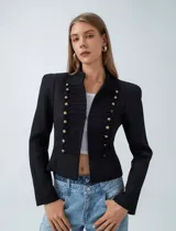 Chaqueta estilo militar color negro, con cuello mao y cierre frontal decorado con cordones trenzados y botones metálicos dorados.