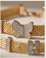 Pulsera de plata 925 con baño de oro, compuesta por una cadena de malla metálica y dijes decorativos, incluyendo una mariposa central con incrustaciones de circonias.