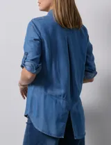 Camisa de tencel color celeste claro, con cuello con solapa, escote en V y abertura central con botones. Manga larga con presilla para ajustar el largo. El largo de espalda es mayor al delantero y tiene un tajo central.