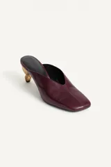 Zapato destalonado tipo mule de piel en color bordó, con escote en pico, punta cuadrada y tacón medio metalizado de diseño escultórico.