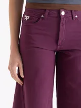 Pantalon de jean color beige, de corte wide leg con silueta redondeada y pinzas en las rodillas. Cuenta con cierre de botón y bragueta, bolsillos laterales y traseros, y detalles de remaches metálicos.