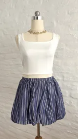 Pollera corta estilo globo, color azul marino con rayas verticales blancas, con cintura elástica.