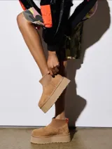 Botas cortas tipo plataforma UGG modelo Mini Dipper, confeccionadas en gamuza color tostado con panel superior de neopreno elástico y tirador naranja en el talón.
