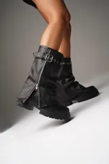 Botas de cuero negras con caña media, base de plataforma y cierre lateral con cremallera. Presentan una correa con hebilla y ojales metálicos en la parte superior de la caña. La caña mide 30 cm y la base 6 cm.