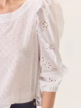 Blusa blanca de algodón con bordado inglés en el frente y las mangas. Presenta volados decorativos a lo largo de las mangas, puños elásticos y espalda de tejido de punto para mayor comodidad.