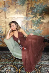 Vestido largo de encaje y transparencias color marrón, con escote profundo halter, frunces en el cuerpo, espalda abierta y tiras largas estampadas para atar al cuello.