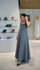 Vestido largo de paño gris con sutiles destellos brillantes, corte entallado en el torso con escote cuadrado y falda amplia con bolsillos laterales.