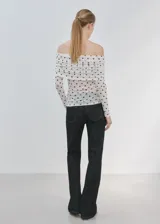 Camiseta blanca de malla con estampado de lunares negros, escote palabra de honor cruzado con fruncidos y manga larga.